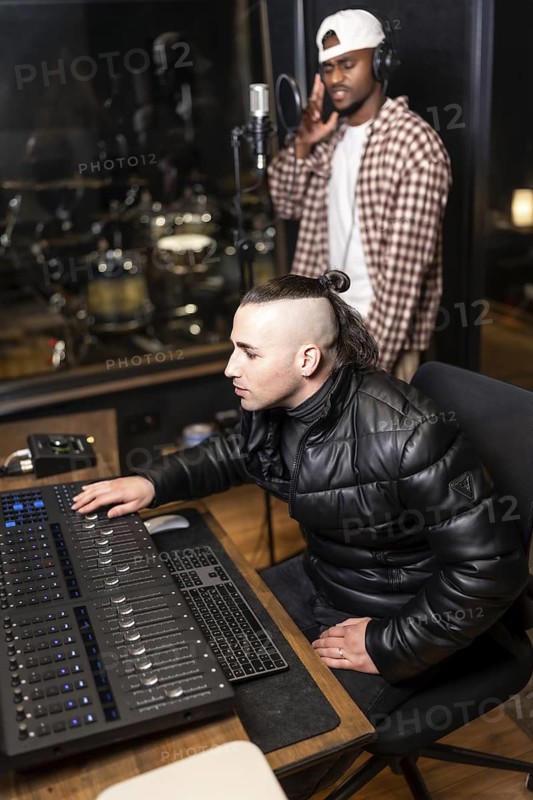 Sound engineer using mixing console while singer recording new pop album in professional music studio