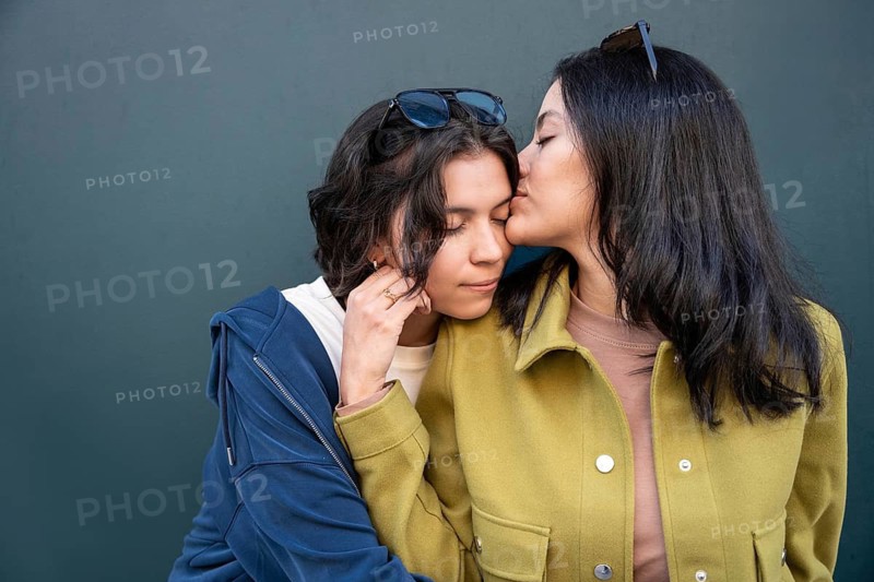 A tender moment between a couple as one partner gently kisses the other's forehead, showing affection and warmth. They are wearing casual clothing with sunglasses