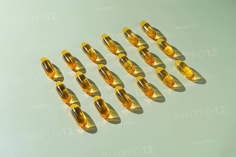 From above multiple omega 3 fish oil capsules neatly aligned in rows on a light green background, emphasizing their golden, translucent quality under soft lighting