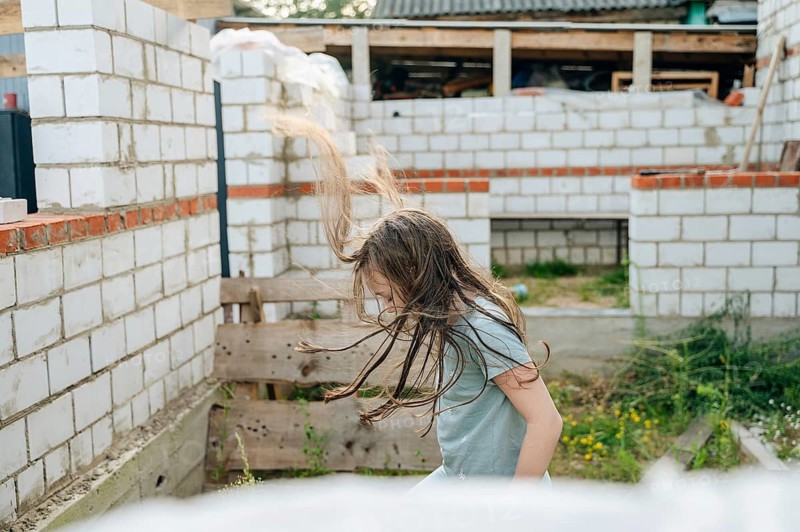 A young girl is joyfully playing amidst the unfinished structures at a construction site, her hair flowing as she moves energetically through the scene