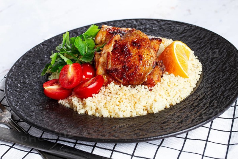 Grilled chicken served with couscous with fresh vegetables and herbs on a black platter, Greek cuisine, homemade
