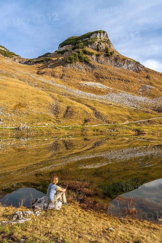 Lake Augstsee and the Atterkogel mountain on the Loser. A hiker sits on a rock. Autumn, good weather, blue sky. Reflection. Altaussee, Bad Aussee, Ausseer Land, Totes Gebirge, Styria, Upper Austria, Austria