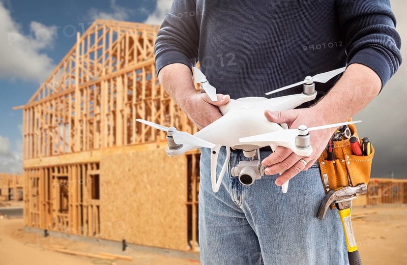 Construction Worker and Drone Pilot With Toolbelt Holding Drone At Construction Site