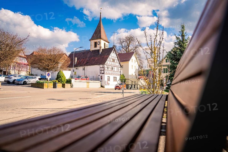 Half-timbered church and half-timbered houses in the city center, with a park bench in the foreground and blue sky, Deufringen, Aidlingen, district of Böblingen, Germany