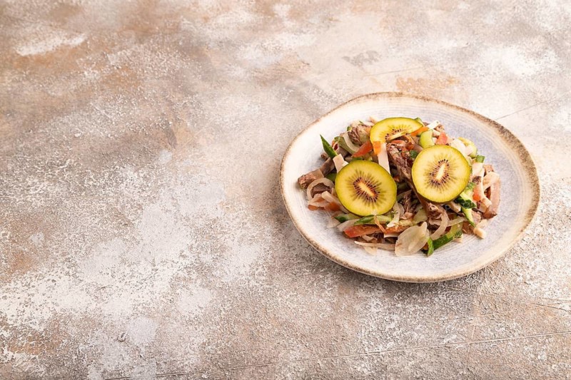 Meat salad with beef kiwi and vegetables on brown concrete background. side view, copy space