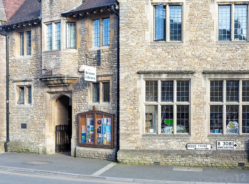 Historic local library building with sign and council noticeboard outside, Bruton, Somerset, England, UK
