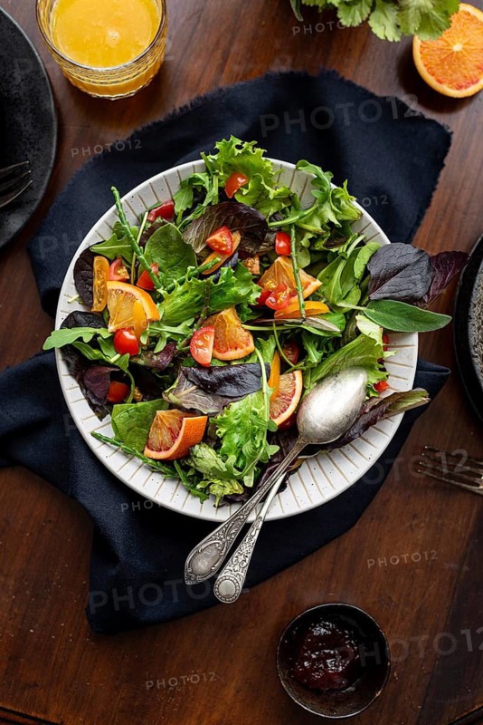A vibrant salad featuring fresh greens, cherry tomatoes, and citrus slices in a white bowl, set on a wooden table. A refreshing and colorful dish perfect for a healthy meal