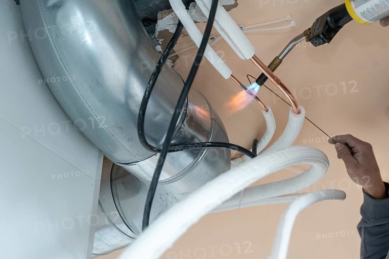 Technician installing a modern hvac system, using a blowtorch to braze copper pipes for an air conditioning unit, ensuring proper function and heating or cooling in a new construction