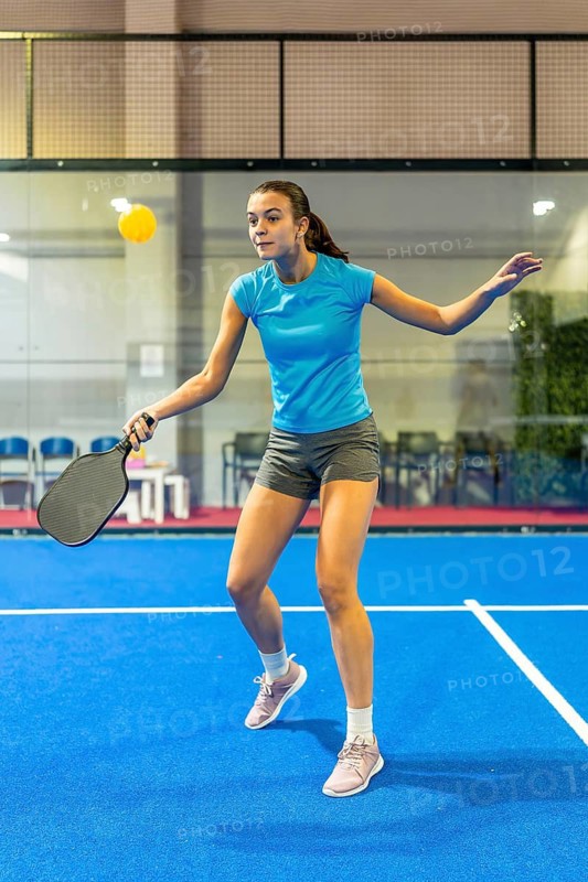 Woman playing pickleball on an indoor court, actively swinging a paddle to hit the ball, demonstrating athleticism and focus during intense competition