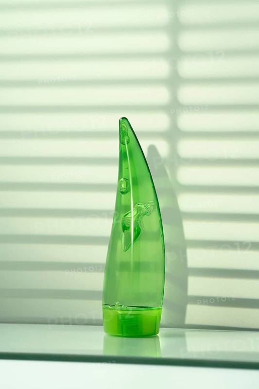 A transparent aloe vera gel bottle is bathed in sunlight, casting soft shadows on a sleek bathroom shelf, hinting at daily skincare routines