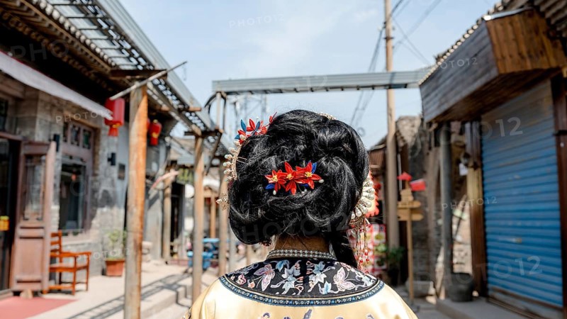 Woman in exquisite Qing dynasty attire adorned with elegant accessories, looking at the camera. Captured in the historic streets of Pingyao, China, showcasing traditional culture