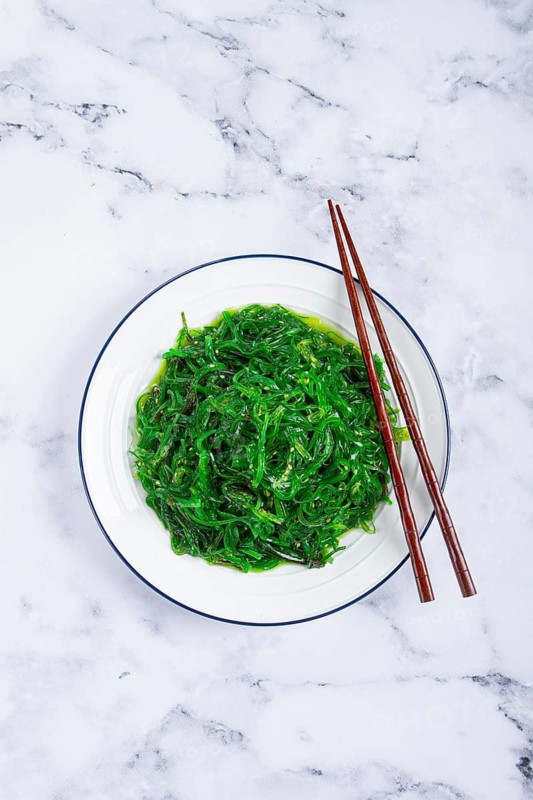 Chuka salad, made from fresh seaweed, with sesame dressing, served on a white plate, with chopsticks, no people