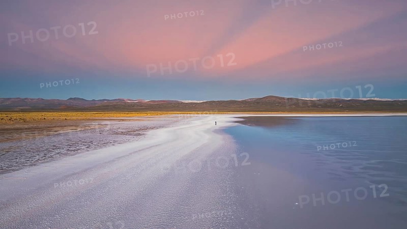 A stunning panoramic view of Salinas Grandes in Salta, Argentina. The salt flats reflect a breathtaking sunset with vibrant pink and blue hues, creating a serene atmosphere