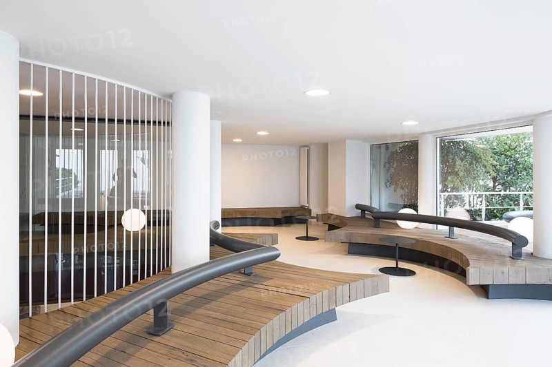 Modern interior in club with curved wooden benches and sleek iron railings. Minimalistic design emphasizes open space and natural light, creating a serene atmosphere