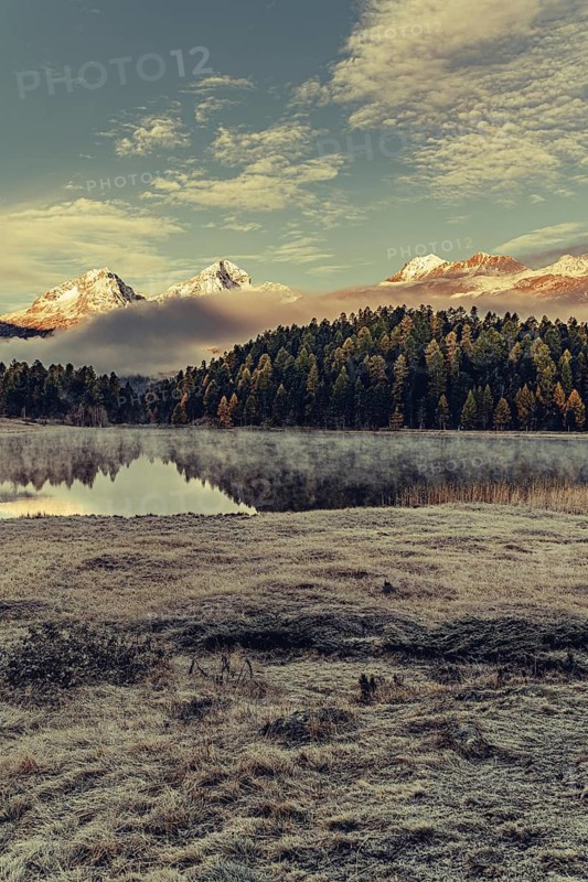 Lake Staz near Sankt Moritz in the Engadin in Switzerland. Morning atmosphere with fog in autumn. Water reflection and snow-covered mountains in the background