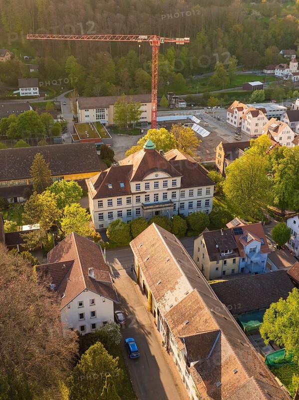 A building complex with a construction crane and surrounding trees in the evening sun, Nagold, Black Forest, Germany