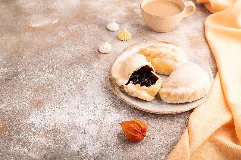 Glazed Pies with blueberry jam on brown concrete background and orange linen textile, cup of coffee, side view, copy space