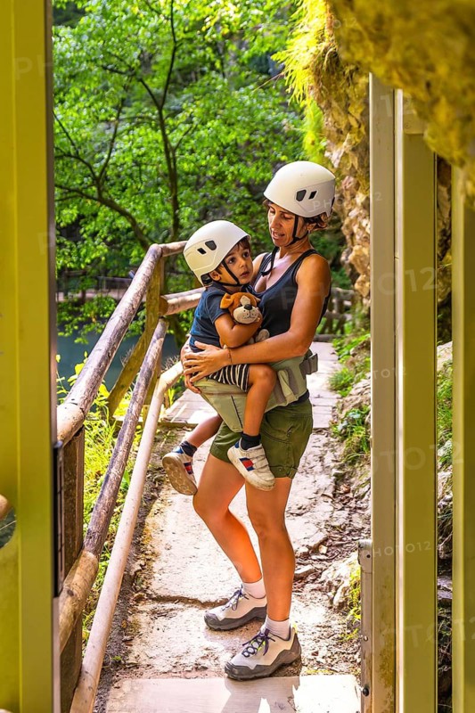 Mother carrying her son while wearing safety helmets during a visit to the scenic vintgar gorge, enjoying a safe and memorable family adventure in nature