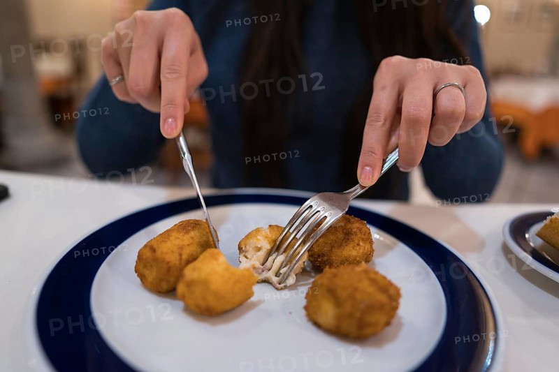 Woman enjoys a plate of croquetas at a rustic Spanish restaurant, surrounded by traditional decor with wooden beams, columns, and an intimate dining atmosphere