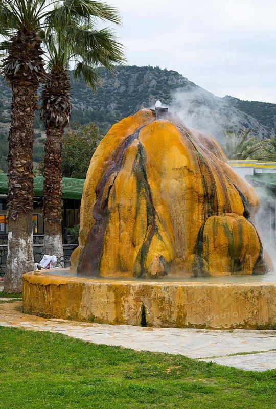 A hot spring with steaming rocks surrounded by palm trees and mountains, Karahayit Kirmizi Su, Red Spring, Pamukkale, Denizli, Turkey