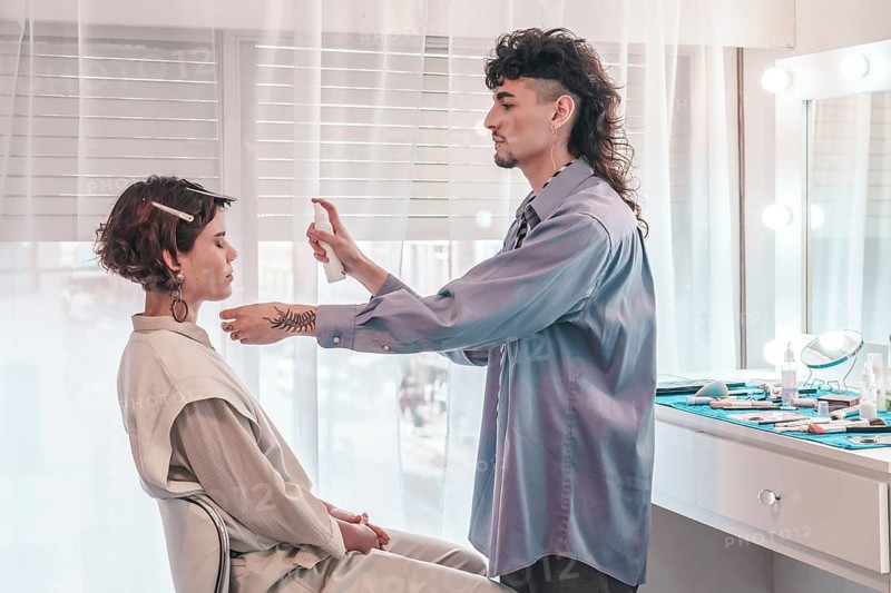 Professional makeup artist spraying a cosmetic product on a model's face, skillfully preparing her for a makeup session in a stylish beauty salon filled with natural daylight