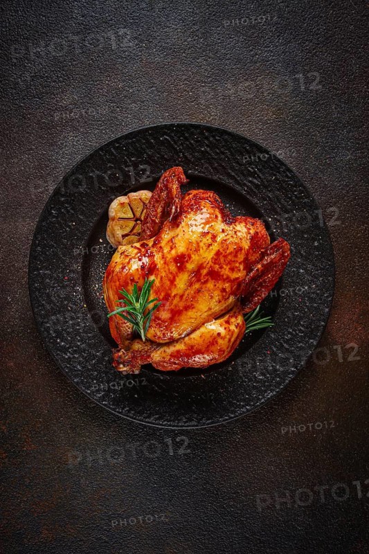 Baked chicken on a black dish with herbs and garlic, on a dark background, homemade, no people