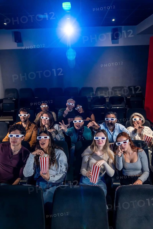 Group of excited friends wearing 3d glasses and eating popcorn while watching a movie in the cinema