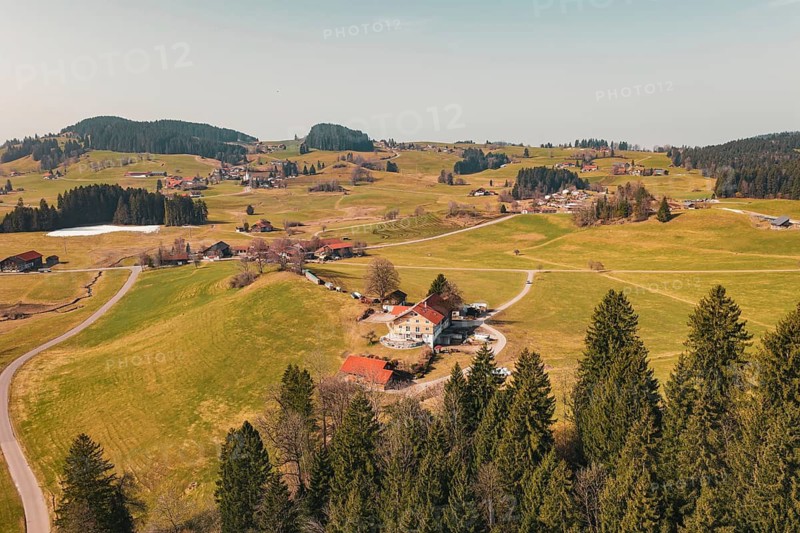An idyllic alpine landscape with scattered buildings and green hills in clear weather, Oberreute, Allgäu, Germany