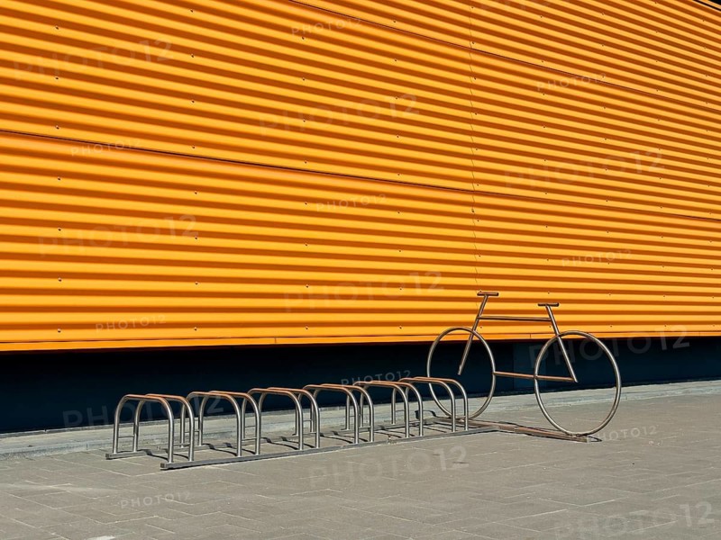 A crisp image showcasing a modern industrial building's vibrant yellow exterior wall, contrasted with a minimalistic metal bike rack and an artistic bike sculpture in sunlight