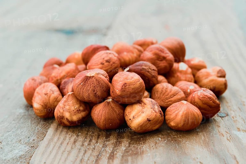 A close-up shot of a pile of fresh hazelnuts resting on a rustic wooden tabletop. The hazelnuts rich brown color contrasts beautifully with the textured wooden surface