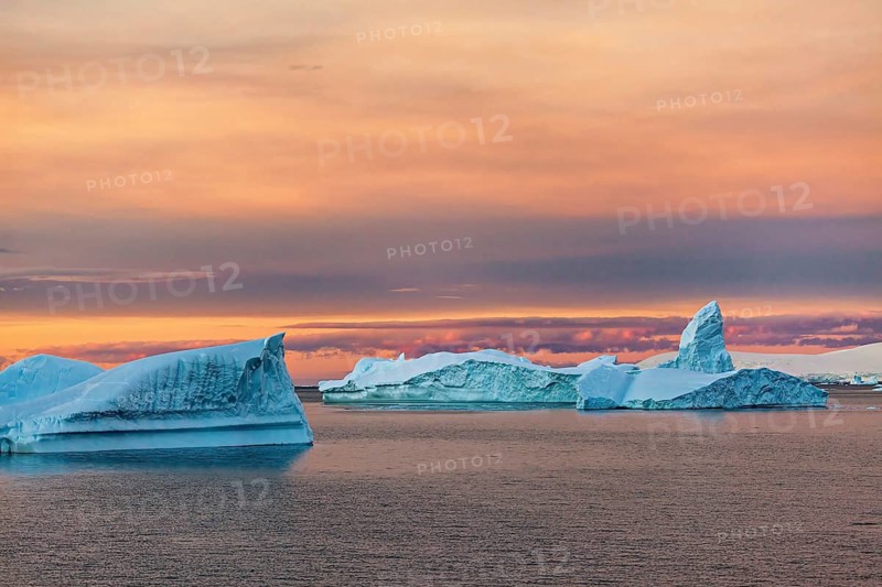 Icebergs in the sea under a warm, colourful sky at sunset, icebergs in the Southern Ocean in Antarctica