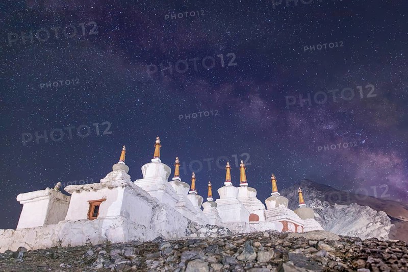 Under a mesmerizing starry sky in Diskit, Nubra Valley, India, ancient white stupas stand majestically, blending history and natural beauty in this serene Himalayan landscape