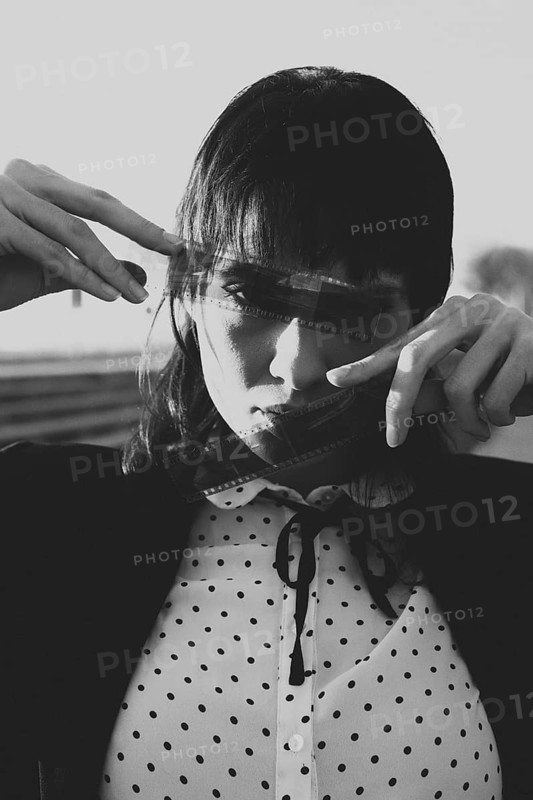 A black and white portrait features a woman holding film strips over her face, creating a vintage effect. The dotted blouse adds a touch of retro style to the artistic composition
