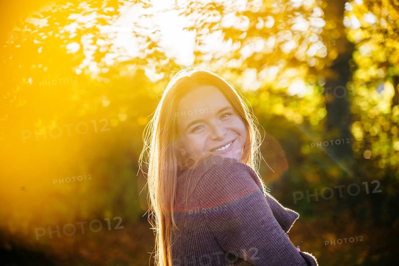 Beautiful pregnant woman with flowing red hair stands gracefully in a natural setting, surrounded by soft sunlight and greenery, embodying serenity and joy in motherhood