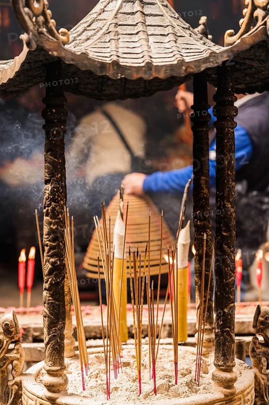 Back view of unrecognizable person participating in a traditional incense burning ceremony at a temple in Hong Kong during Chinese New Year. The image captures a spiritual ambiance with smoke and ritual details