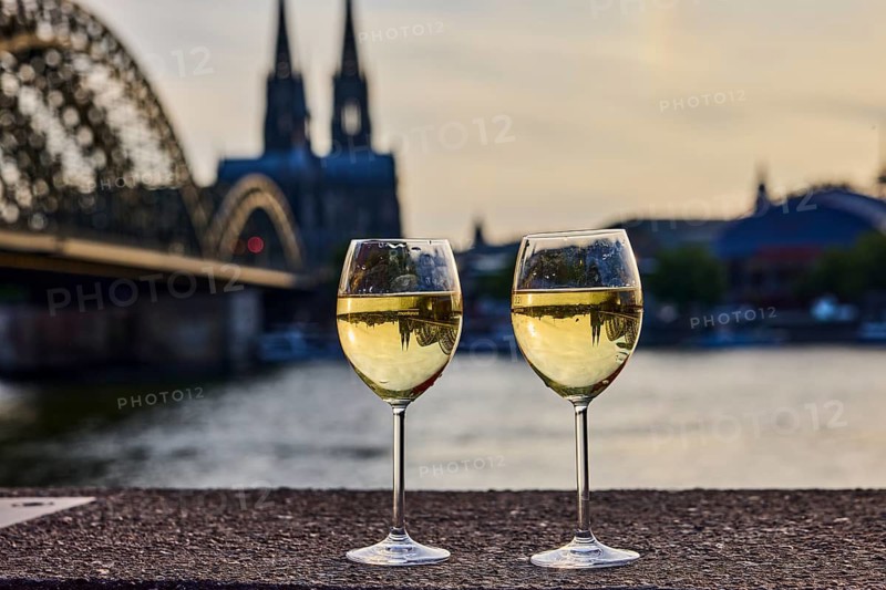 Wine glasses, wine, light refraction in filled glasses, concrete wall, Rhine river, Hohenzollern bridge, arched bridge, steel arches, Cologne Cathedral, double tower, general architecture, depth of focus, sharp foreground - background blurred, sunset, red and orange sky, cirrostratus clouds, Cologne, district-free city, North Rhine-Westphalia, Germany