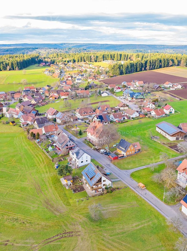 View from above of a small village with fields and houses in an open, green landscape with a cloudy sky, Agenbach, Black Forest, Germany