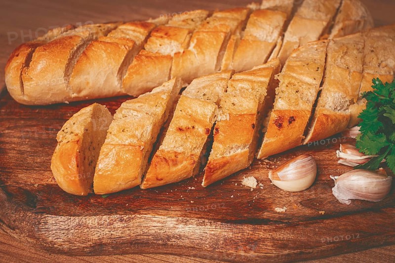 Garlic bread, baguette with garlic butter and herbs, on a wooden board, with herbs and garlic cloves