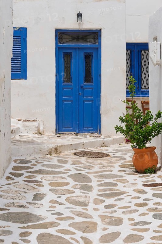 Idyllic Mediterranean scene with blue door, white walls and clay pot on cobbled alley, alley in the old town of Parikia, Paros