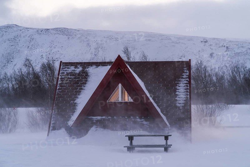 Cozy A-frame cabin nestled amidst the snowy wilderness of Swedish Lapland. The serene winter landscape with frost-covered branches highlights the tranquility of nature