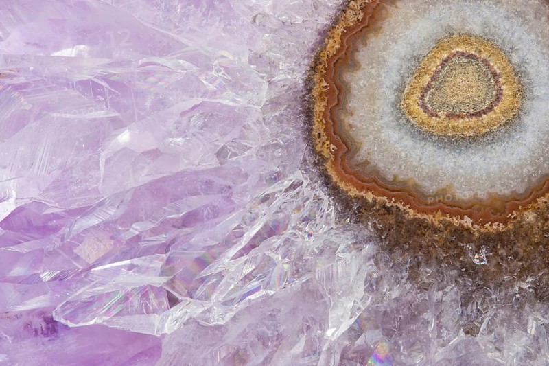 Detailed macro image of an amethyst stalactite slice, featuring sparkling purple crystals radiating from an agate and chalcedony core, showcasing intricate natural textures and layers