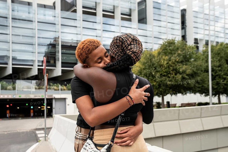 An LGBT multiethnic couple shares an affectionate embrace in an urban setting, showcasing love and diversity. They are captured in a moment of true connection and joy