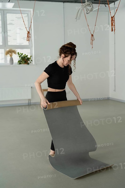 A woman rolls out a yoga mat in a minimalistic studio. She is in casual attire, creating a calming and focused atmosphere for exercise or meditation