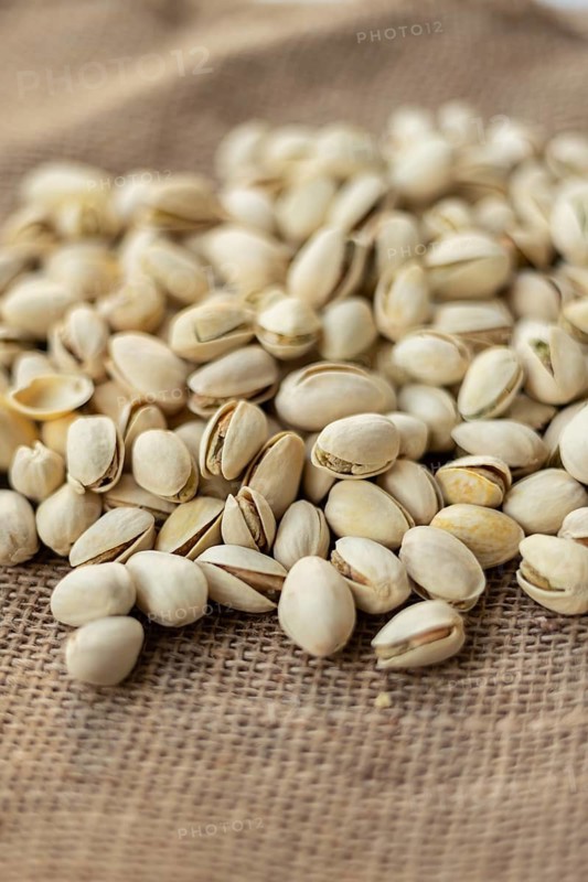 A pile of pistachios lies scattered on a rustic burlap surface, showcasing their textured shells. The focus on the nuts highlights the natural texture and earthy tones