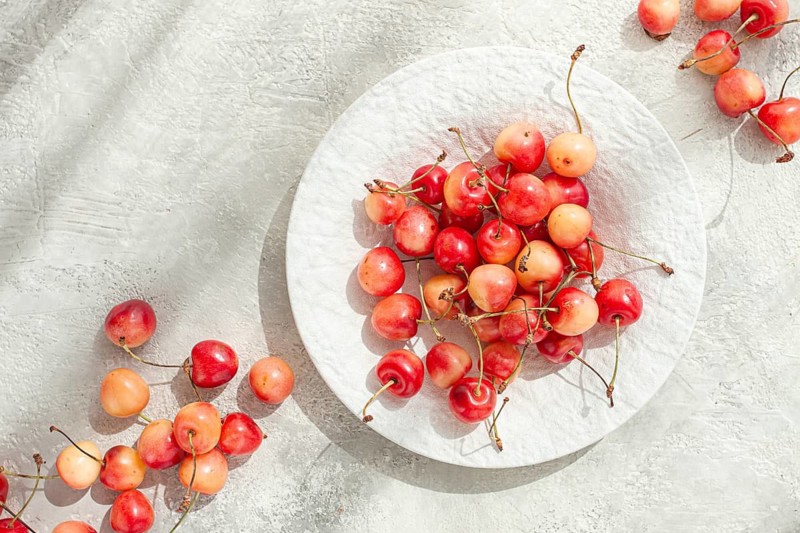Yellow cherries on a white platter, scattered on the table, natural light, top view