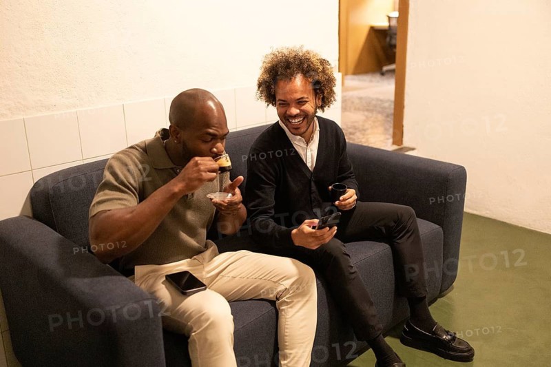 Professionals enjoy a relaxed coffee break on a couch during a coworking session in Barcelona. They chat and laugh, blending work with social interaction in a cozy space