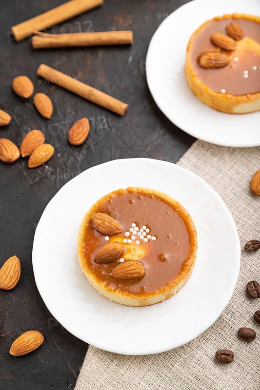 Sweet tartlets with almonds and caramel cream with cup of coffee on a black concrete background and linen textile. Top view, close up, selective focus