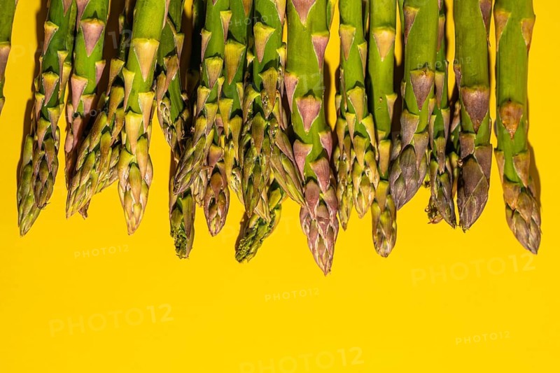 A close-up of fresh green asparagus spears displayed against a vibrant yellow background, highlighting their natural texture and color, ideal for culinary or health themes