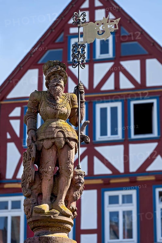 Market fountain man with market flag, knight, sandstone sculpture, fountain figure at the Kump, medieval market fountain, high half-timbered houses on the market square, historic old town, Butzbach, Wetterau, Hesse, Germany