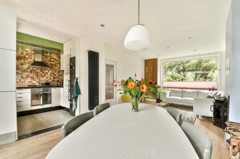 Bright open concept kitchen and living area featuring a modern design. A cozy living room with a large window complements the white dining table with fresh flower centerpiece